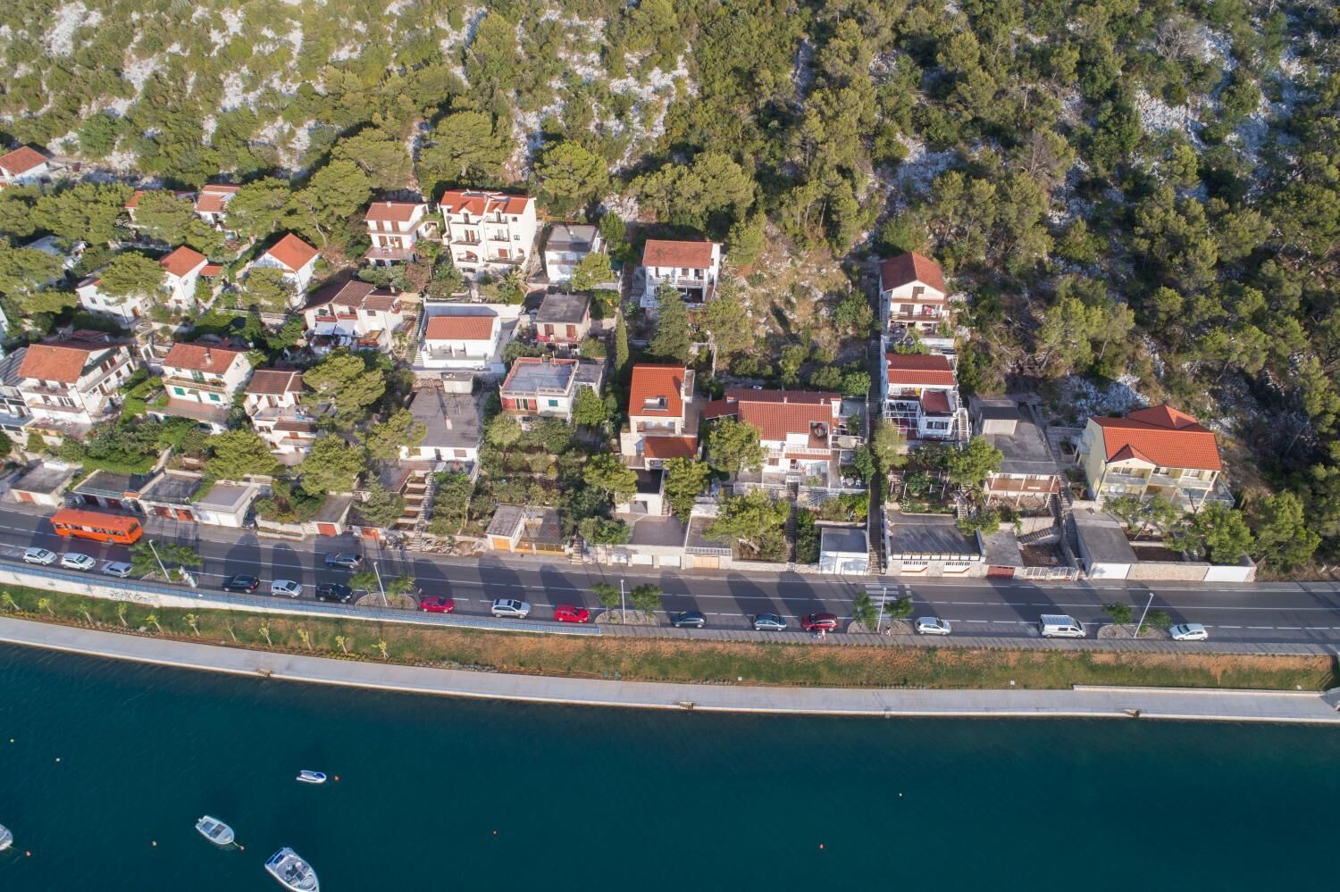 An aerial view of a coastal residential area with houses, a road, and a marina with boats.