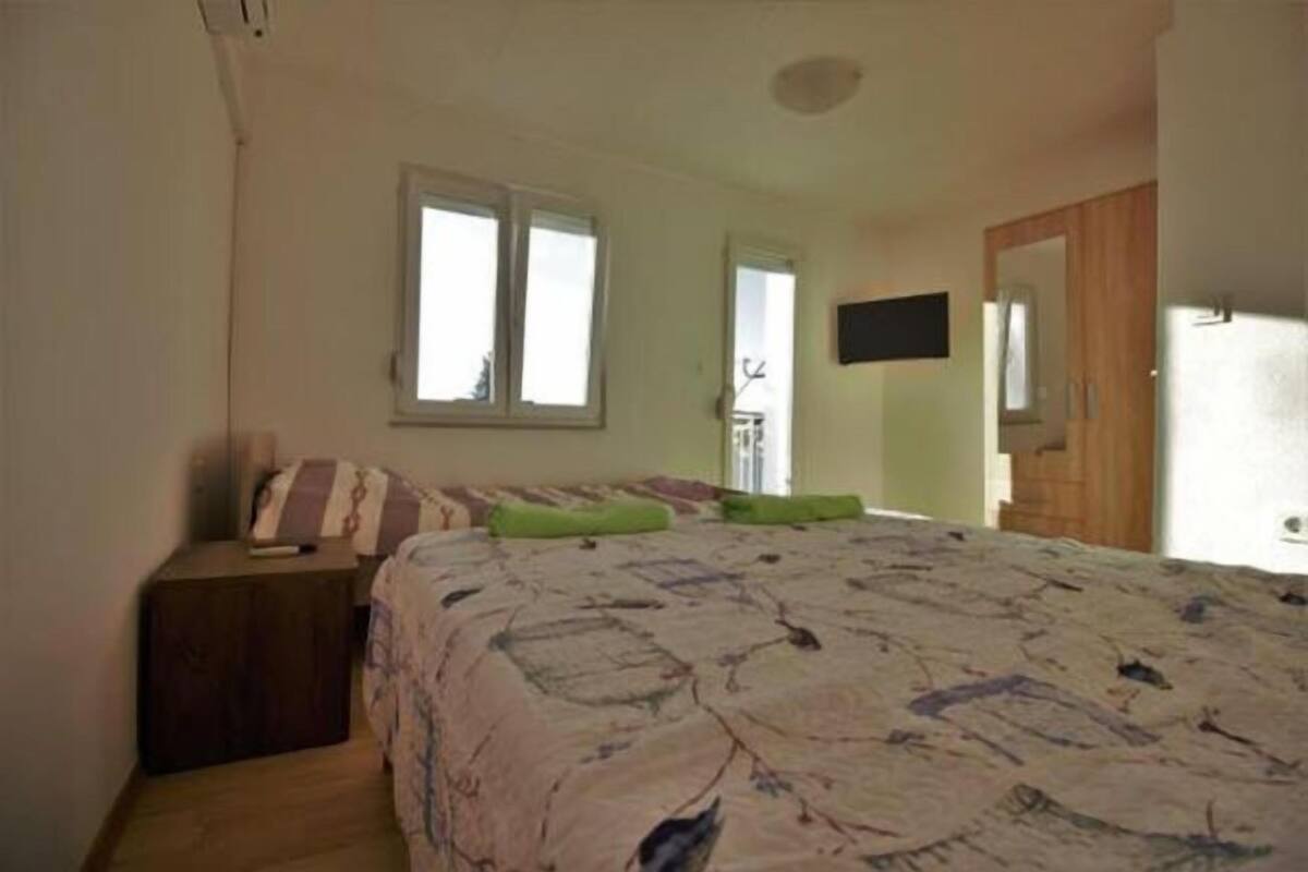 Une chambre à coucher avec un lit, une table de chevet, un téléviseur fixé au mur et une fenêtre.