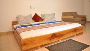 Una camera da letto con un letto di legno, biancheria a motivi, un cuscino rosso e una poltrona beige.