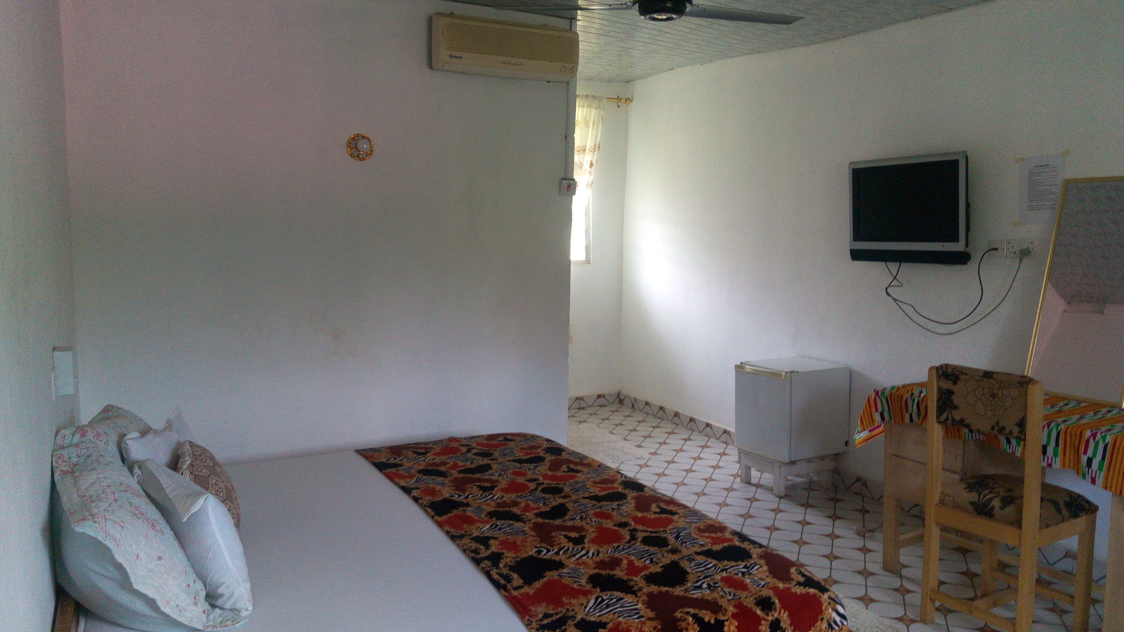 Una habitación pequeña y sencilla con cama, una silla, televisor y refrigerador.