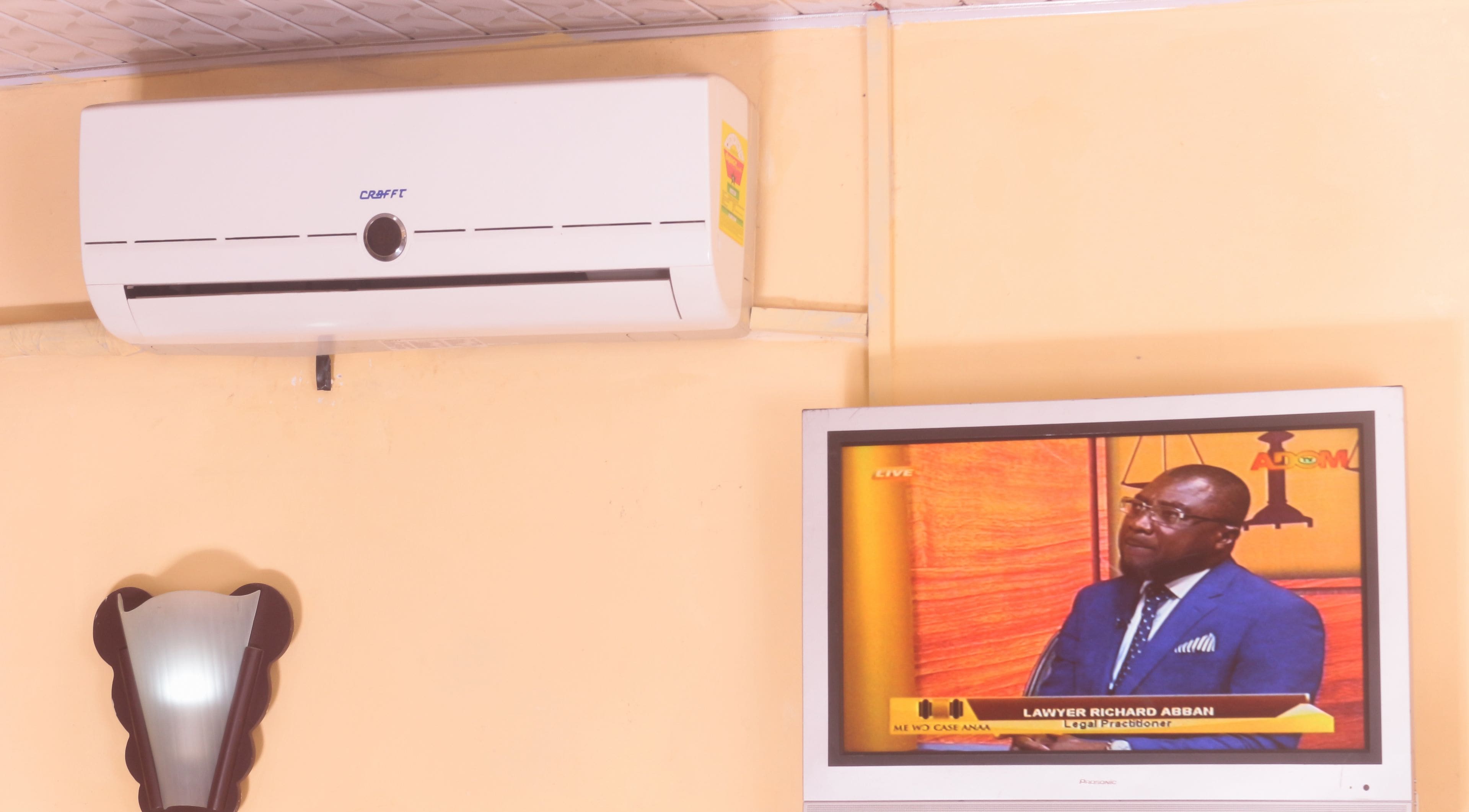 A room with a mounted air conditioner and a television displaying a news program.