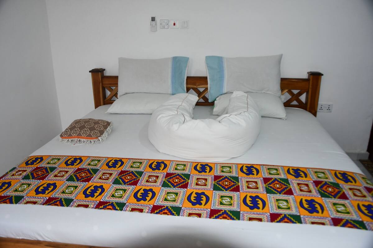 A bed with a patterned blanket, pillows, and a decorative pillow.