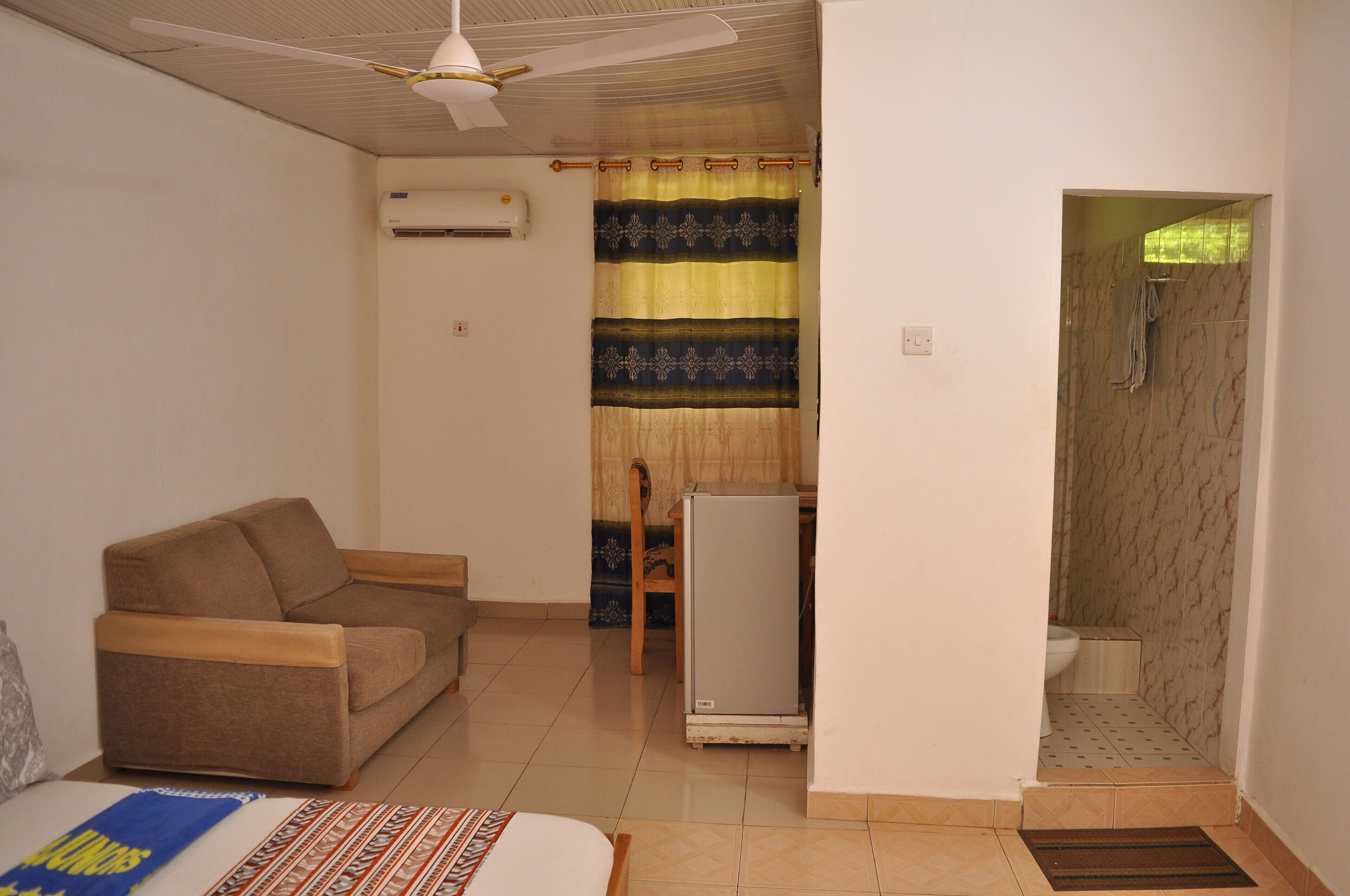 Una habitación pequeña y funcional con sofá, refrigerador y zona de ducha.