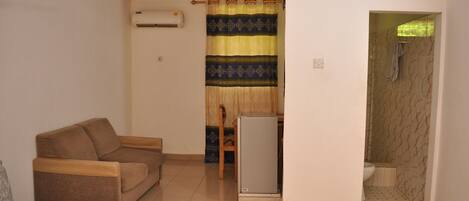 A small, compact room with a sofa, a refrigerator, and a shower area.