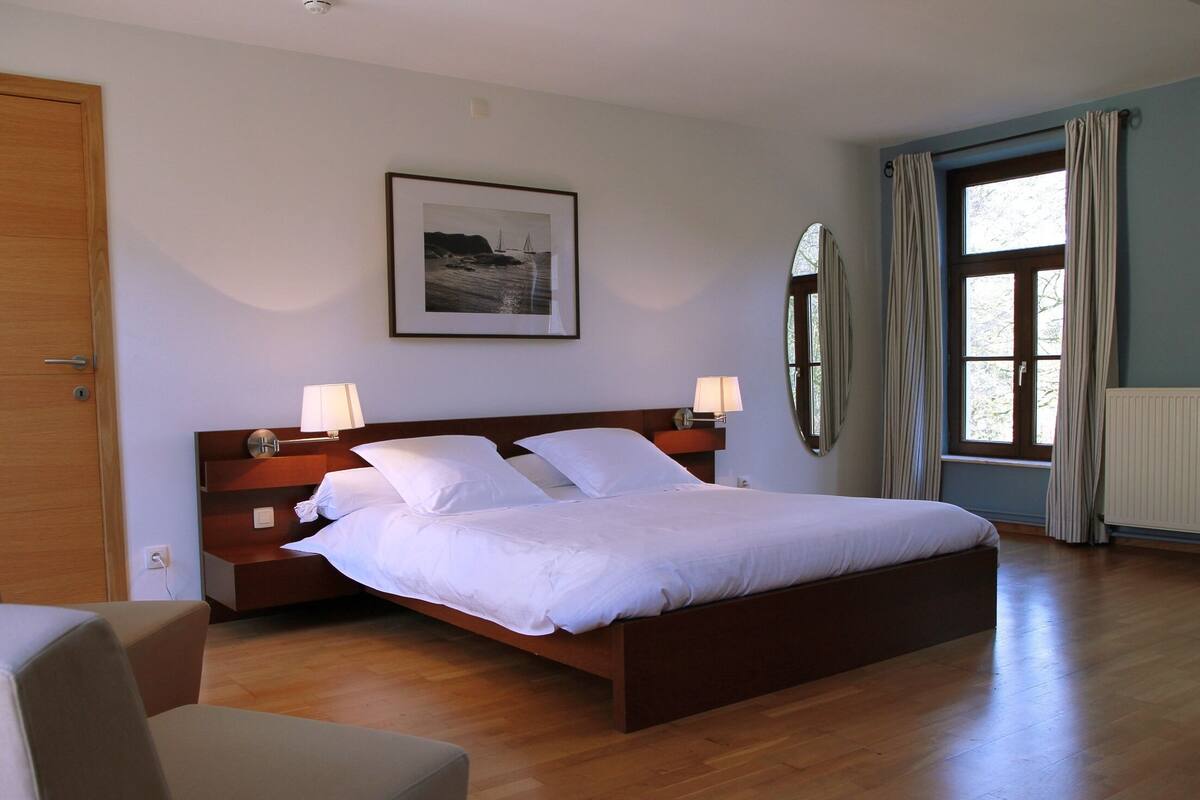 Una habitació ben ordenada amb un llit gran, làmpades de nit, un quadre al mur i una finestra amb cortines.