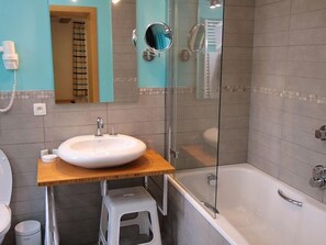 Un baño con un lavamanos blanco, un mueble de tocador de madera, una mampara de vidrio para la ducha y un inodoro blanco.