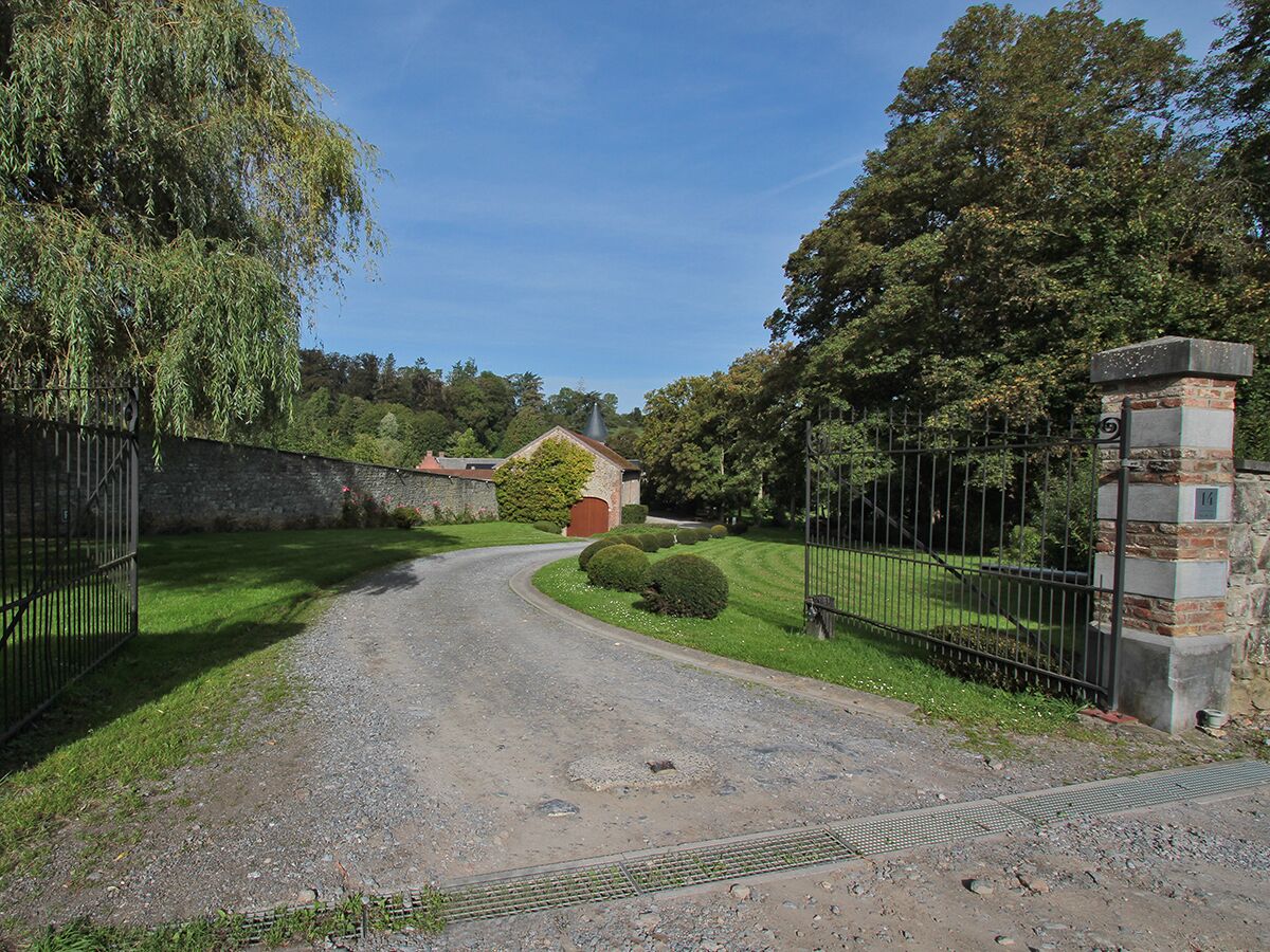 A gravel driveway leading to a gated entrance with a brick pillar and a metal fence.
