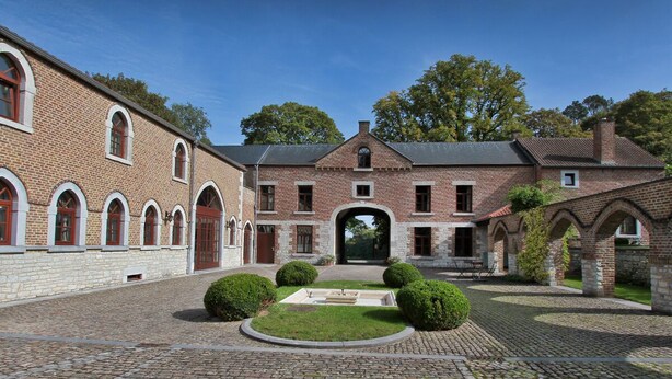 Ein Innenhof mit einem Backsteinhaus, einem Steinweg und ordentlich geschnittenen Büschen.