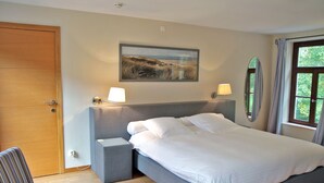 Ein Schlafzimmer mit Bett, Nachttischen, einem Sessel, einem Gemälde und einem Fenster mit Vorhängen.