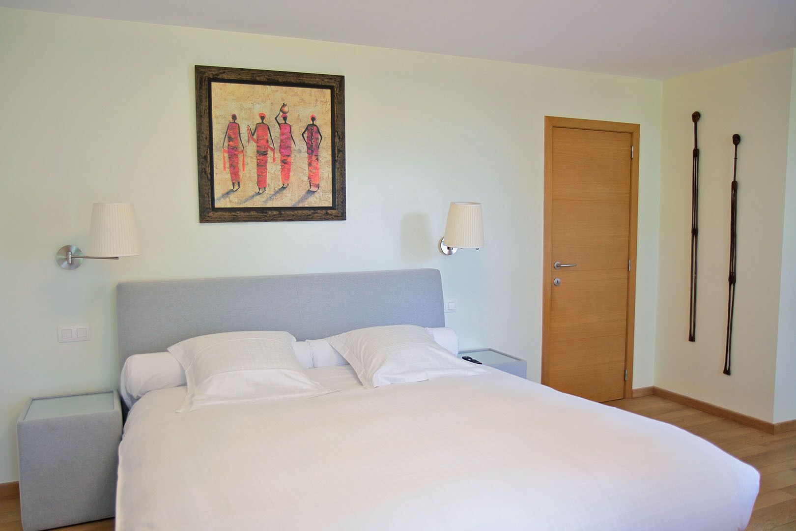 Un dormitorio con cama, lámparas de noche, una puerta de madera y un cuadro en la pared.