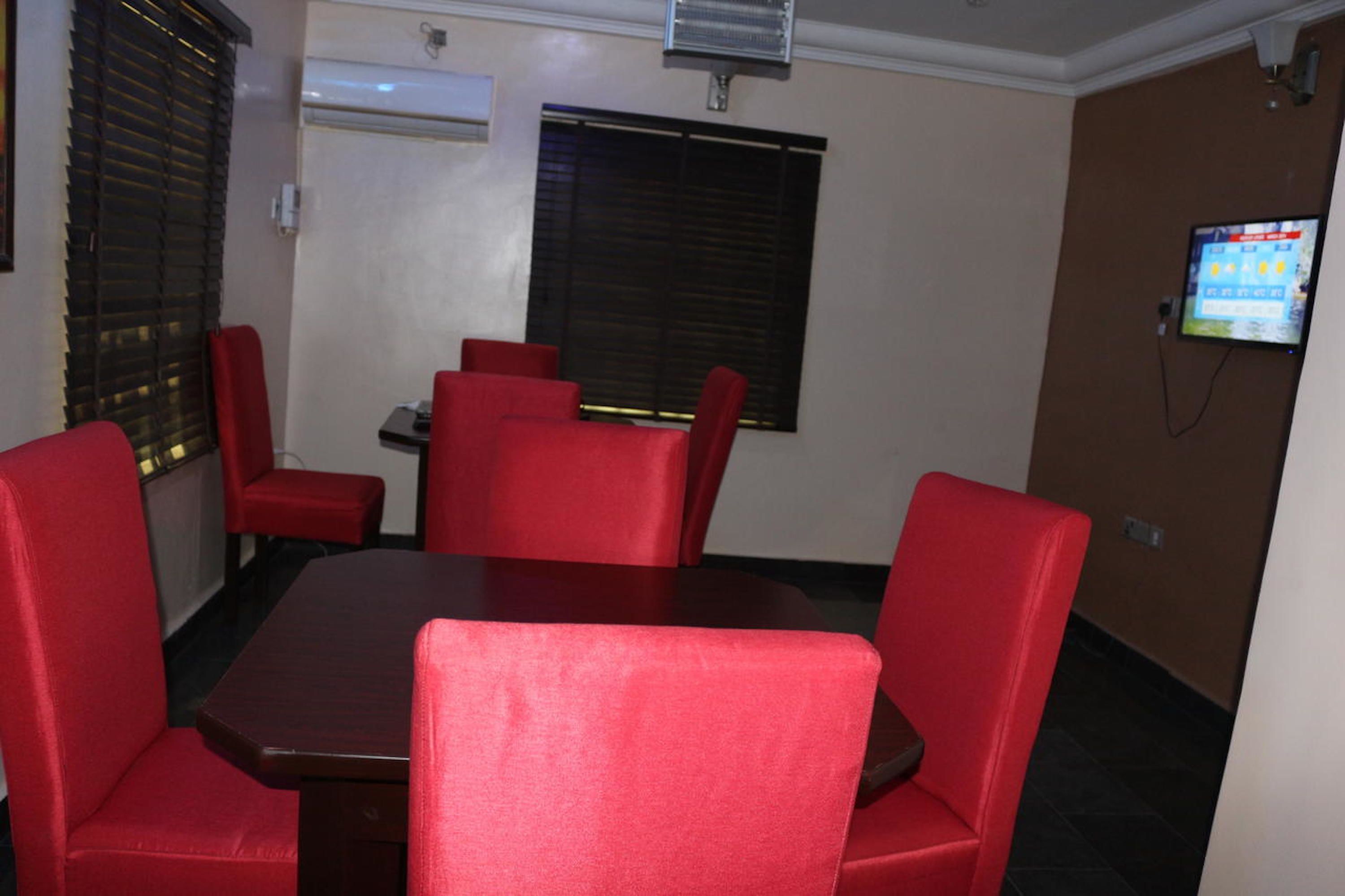 Un salón de conferencias con una mesa rectangular y seis sillas tapizadas rojas.
