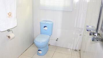Um banheiro com vaso sanitário azul, uma toalha branca pendurada na parede e uma janela com persianas.