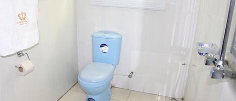 A bathroom with a blue toilet, a white towel hanging on the wall, and a window with blinds.