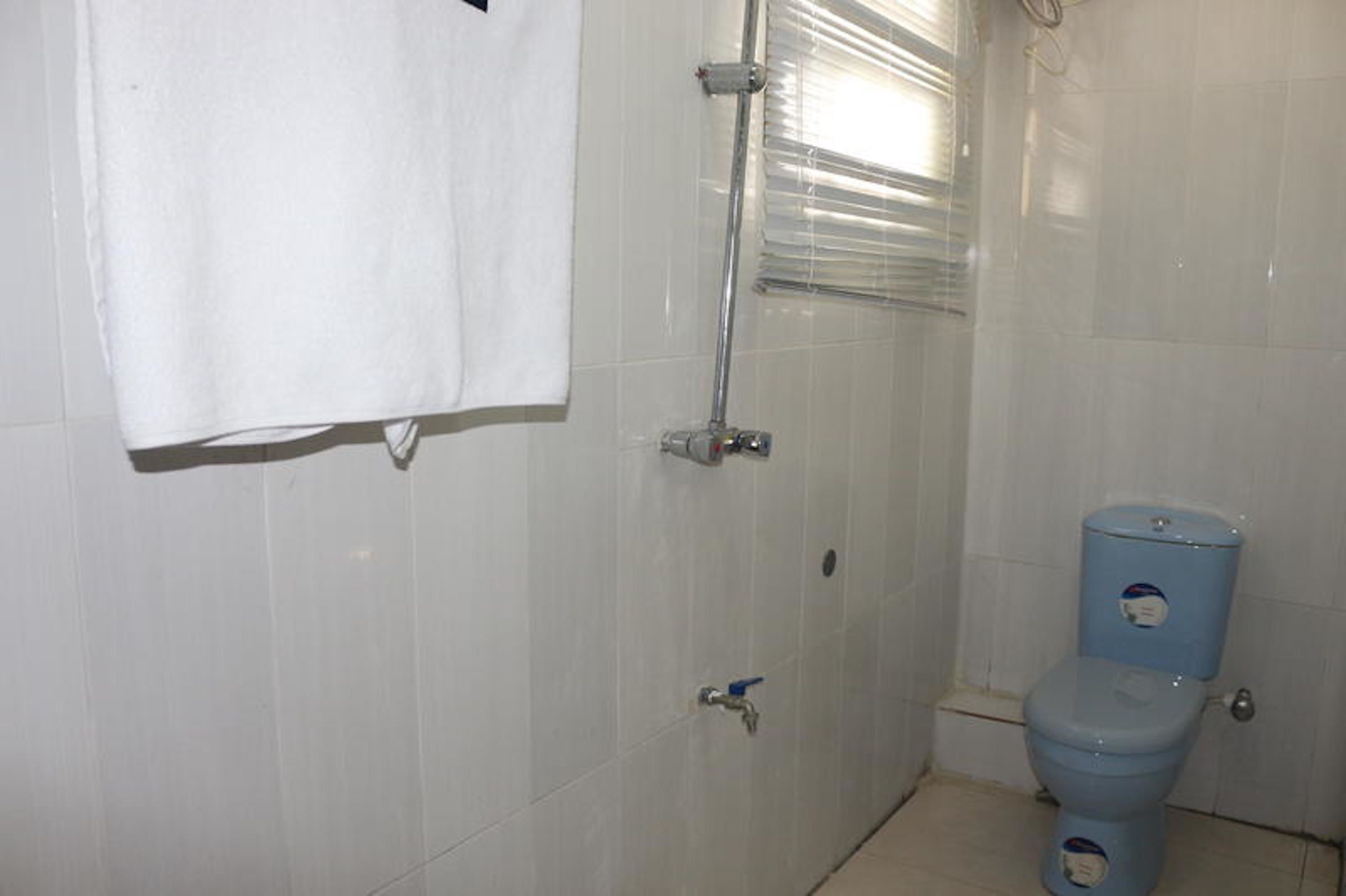 Ein Badezimmer mit weißen Fliesen, einem weißen Handtuch an der Wand, einer blauen Toilette und einer Dusche mit Glastür.