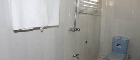 A bathroom with white tiled walls, a white towel hanging on the wall, a blue toilet, and a shower with a glass door.