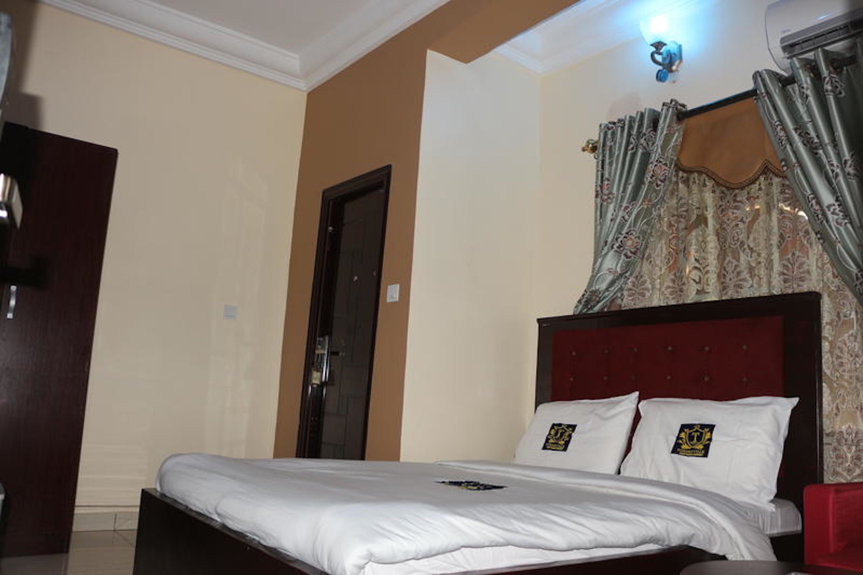 A hotel room with a large bed, a wooden headboard, and a window with patterned curtains.