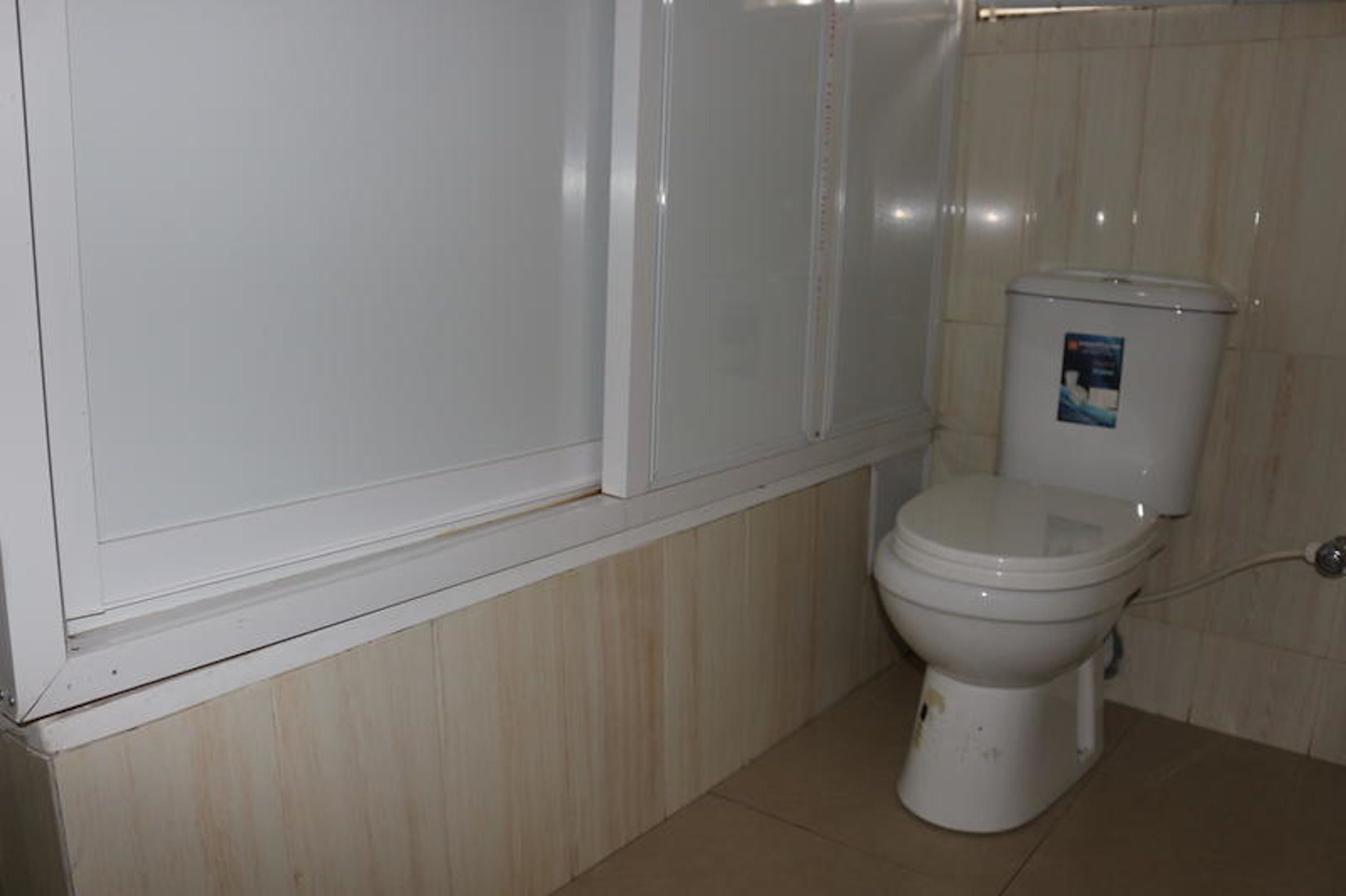 Un baño con inodoro, cabina de ducha blanca y paneles de madera en la mitad inferior de las paredes.