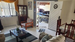 Un salon comprenant un canapé, un fauteuil, une table basse et une porte donnant sur un garage où se trouve une voiture.