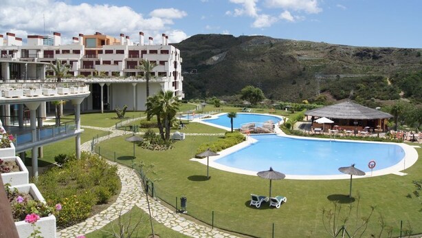A resort with a pool area, lounge chairs, and a building with multiple floors. - Parque Botanico Holiday Rentals (Estepona)