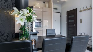 Een moderne eetruimte met een zwarte tafel en stoelen, een vaas met witte bloemen, en een keuken op de achtergrond.