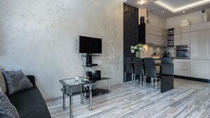 Een moderne woonkamer met een glazen salontafel, een bank en een aan de muur bevestigde televisie.