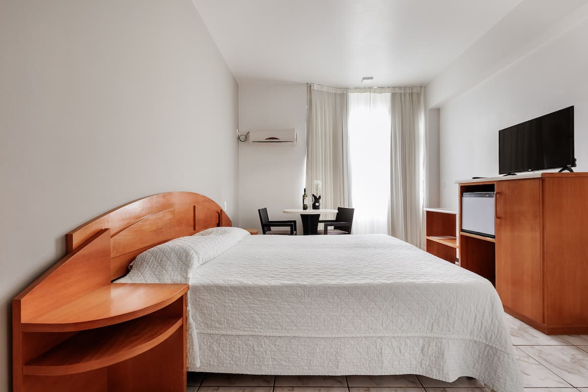 A hotel room with a bed, a wooden headboard, a TV, a desk, and a chair.