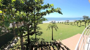 A balcony with a view of a grassy area, palm trees, and a beach in the distance. - Flamboyant Hotel (Barra Velha)
