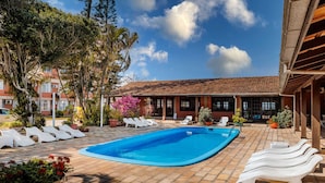 A swimming pool with lounge chairs, surrounded by potted plants and trees. - Flamboyant Hotel (Barra Velha)