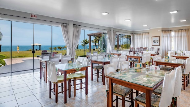 A restaurant with a view of the ocean, featuring tables and chairs with white tablecloths and glass tops. - Flamboyant Hotel (Barra Velha)