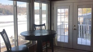A room with a round table and chairs, large windows, and a wooden ceiling. - Winnipesaukee - Lakefront house includes slip, deck, kayaks & sleeps up to 11 (Alton)