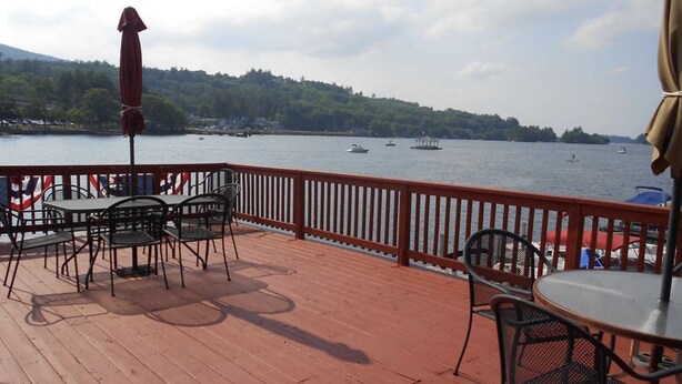 A deck with tables and chairs overlooking a lake with boats. - Winnipesaukee - Lakefront house includes slip, deck, kayaks & sleeps up to 11 (Alton)