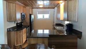 A kitchen with wooden cabinets, a black countertop, and a window. - Winnipesaukee - Lakefront house includes slip, deck, kayaks & sleeps up to 11 (Alton)