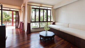 Ein geräumiges Zimmer mit Holzboden, einem großen Fenster mit Vorhängen, einem weißen Sofa und einem kleinen Tisch mit einer Vase.
