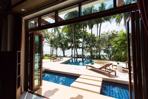 Un espace piscine avec des chaises longues et une vue sur les palmiers et la mer.