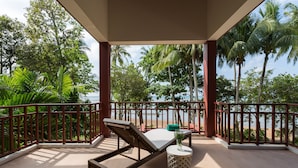 Ein Balkon mit Liegestuhl und Tisch mit Blick auf einen Strand und Palmen.