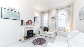 A living room with a fireplace, white sofas, a colorful rug, and framed artwork on the walls. - Spacious Apartment in Trendy Islington (London)
