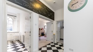 A hallway with a black and white checkered floor, white doors, and a wall-mounted clock. - Spacious Apartment in Trendy Islington (London)