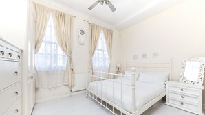 A white bedroom with a bed, dresser, and a mirror. - Spacious Apartment in Trendy Islington (London)