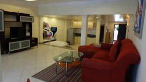 A spacious living room with a red sofa, a glass coffee table, and a modern kitchen in the background.