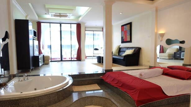 A hotel room with a large bed, a separate bathroom with a bathtub, and a view of the outdoors through the sliding glass doors.