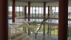 A spacious atrium with a central staircase, large windows, and a view of greenery outside. - Parque Botanico Holiday Rentals (Estepona)