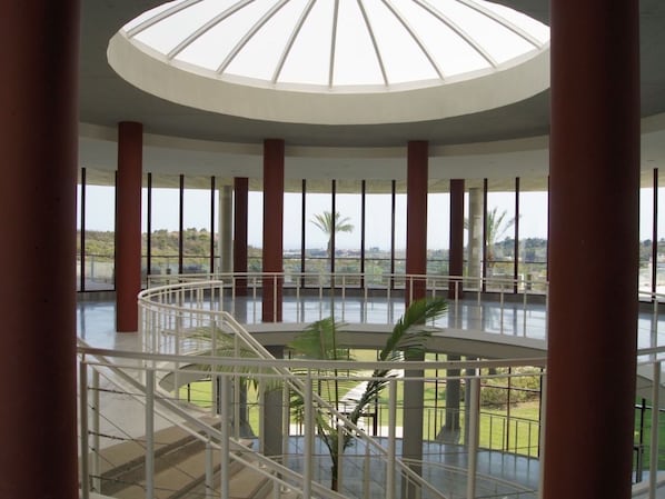 A spacious atrium with a central spiral staircase, large windows, and a view of the outdoors. - Parque Botanico Holiday Rentals (Estepona)
