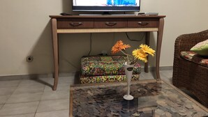 Un escritorio de madera con una televisión, una caja estampada y un florero con flores sobre una mesa de vidrio.