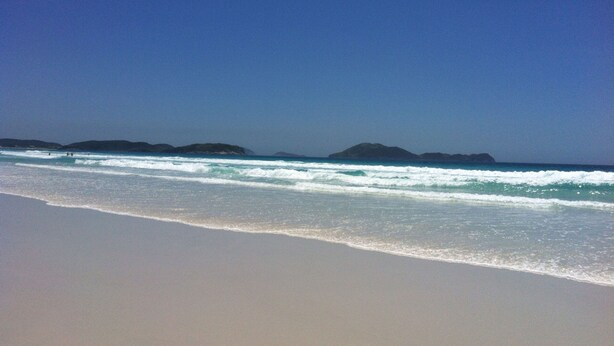 Una playa con agua azul cristalina y islas a lo lejos.