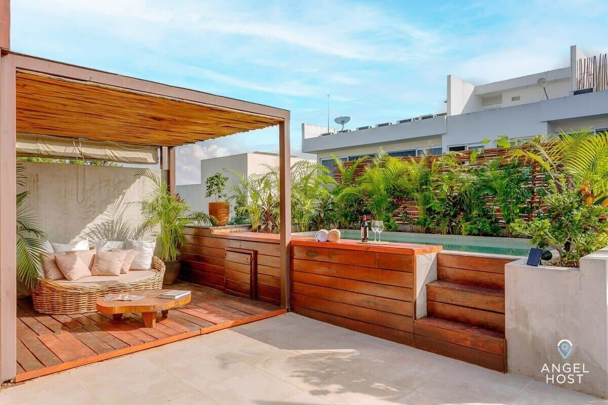 A modern outdoor patio with a wooden bench, a wicker sofa, and a pool.