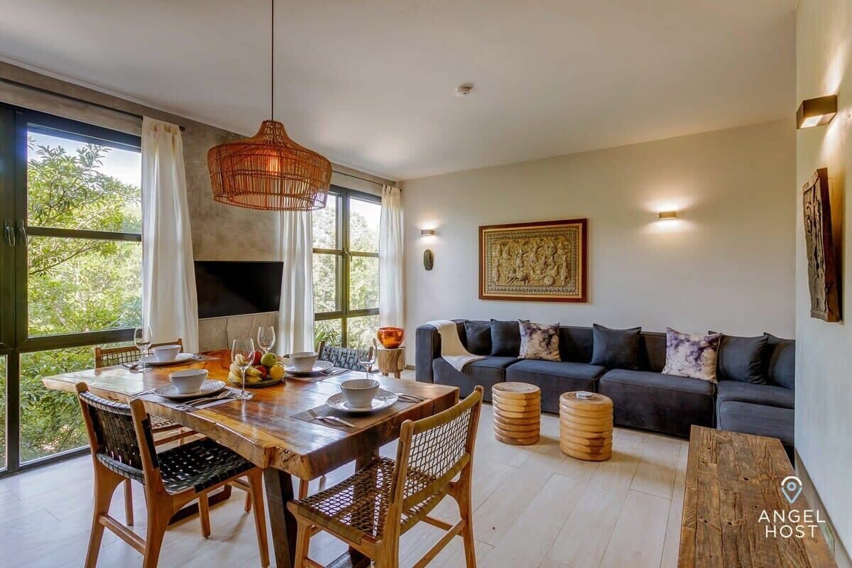 A dining area with a wooden table and chairs, a hanging light fixture, and a sofa with cushions.