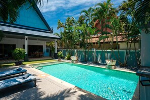 A swimming pool with lounge chairs, surrounded by palm trees and a building with a blue roof.