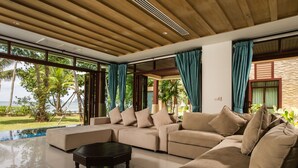 Ein modernes Wohnzimmer mit einer großen Eckcouch, einem Couchtisch und Blick auf einen Pool und eine tropische Landschaft.