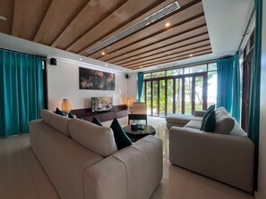 A modern living room with a wooden ceiling, large windows with curtains, and a flat-screen TV on a stand.