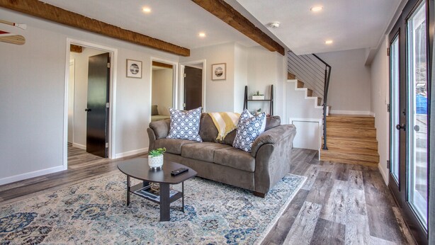 A spacious living room with a brown sofa, patterned rug, and a staircase leading to another level. - 4 BD Entire House Located Close to Downtown and Little Italy! (San Diego)